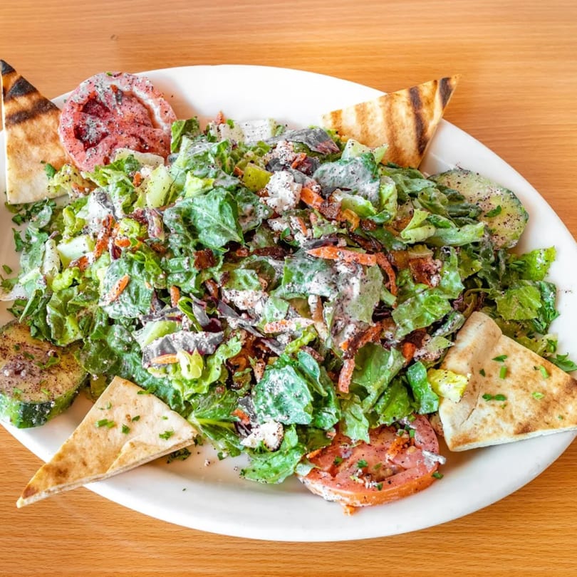 A Fanoos Grill salad with lettuce, tomatoes, avocado, and pita bread on a white plate.