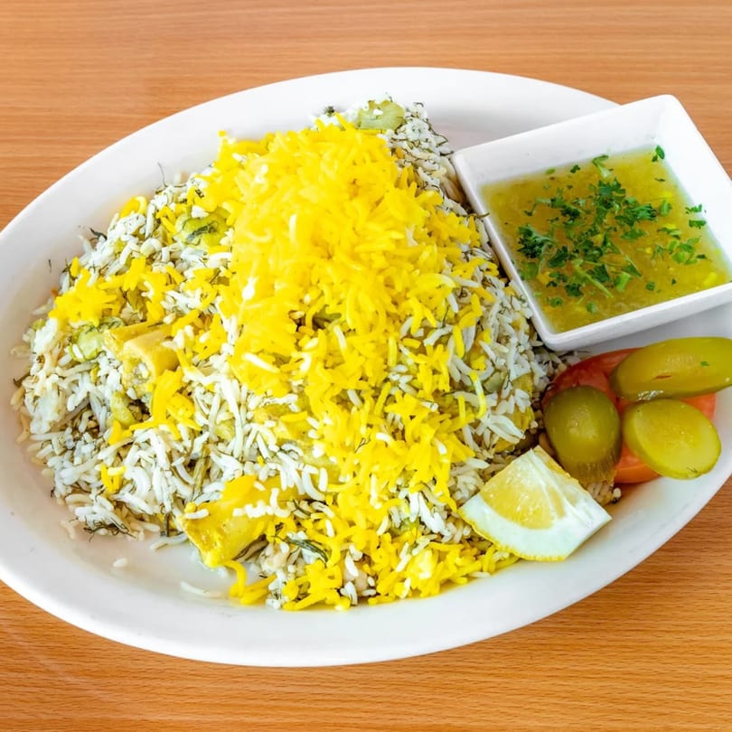 Fanoos Grill's Persian dish with white and yellow rice, a side of sauce, pickles, and a lemon wedge.