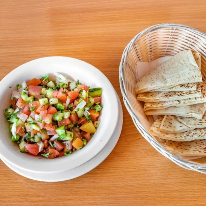 A white bowl of Shirazi salad with diced tomatoes, cucumbers, and onions, next to a basket of flatbread.